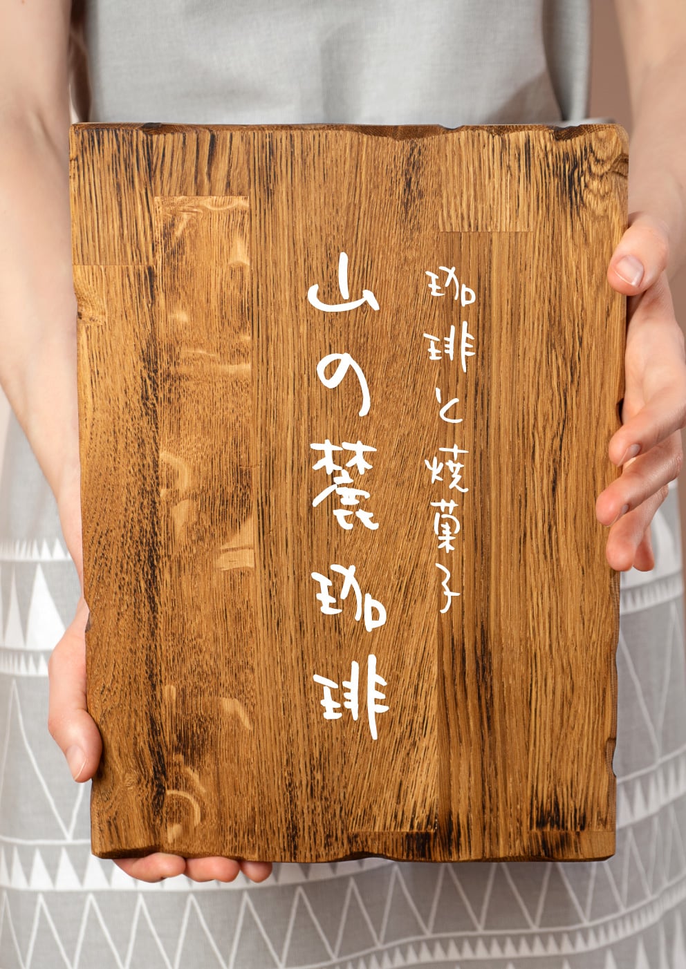 カッティングシートが貼られた木製看板を女性が手に持っている写真